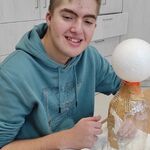 Uczeń okleja kształt zająca z butelki i kuli styropianowej kawałkami gazety.