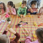 Dzieci siedzą wokół stołu i wykonują ozdoby wielkanocne.