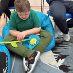 Uczeń siedzi na pufie i patrzy na kwiatek leżący na kolanach.