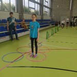 Uczniowie na sali gimnastycznej. Uczennica stoi w kółku, obok jest opiekun.