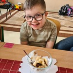 Uczeń siedzi za stołem. Przed nim stoi pucharek z płatkami i owocowymi dodatkami.