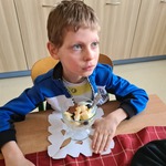 Uczeń siedzi za stołem. Przed nim stoi pucharek z płatkami i owocowymi dodatkami.