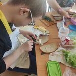 Uczeń siedzi przy stoliku i smaruje chleb masłem. Przed nim na stole leżą produkty do przygotowania kanapek.