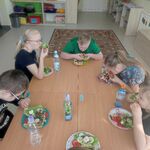 Uczniowie siedzą wokół stołu i jedzą przygotowane przez siebie kanapki z nowalijkami.