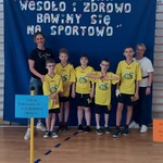 Grupa uczniów z nauczycielkami na tle napisu - Integracyjna Olimpijka WESOŁO I ZDROWO BAWIMY SIĘ NA SPORTOWO