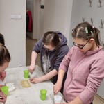 Uczniowie stoją przy stole  i mieszają gips w plastikowych kubeczkach.