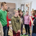 Grupa uczniów w sali muzealnej słucha mówiącej do nich edukatorki.
