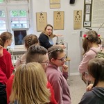Grupa uczniów obserwuje edukatorkę wskazującą eksponat.