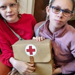 Dwie uczennice siedzą na łóżku i  trzymają po środku torbę z czerwonym krzyżem.