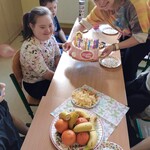 Uczniowie siedzą przy stoliku. Nauczycielka trzyma tort.