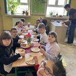 Uczniowie siedzą przy stole, przed nimi są talerze z tortem. Przy biurku opiekun kroi tort.