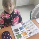 Uczennica siedzi przy stole. Przed nią leży duży zeszyt z wklejoną kartą pracy z pojemnikami na śmieci.