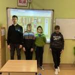 Uczniowie stoją na tle tablicy interaktywnej z wyświetlonym tematycznym slajdem.