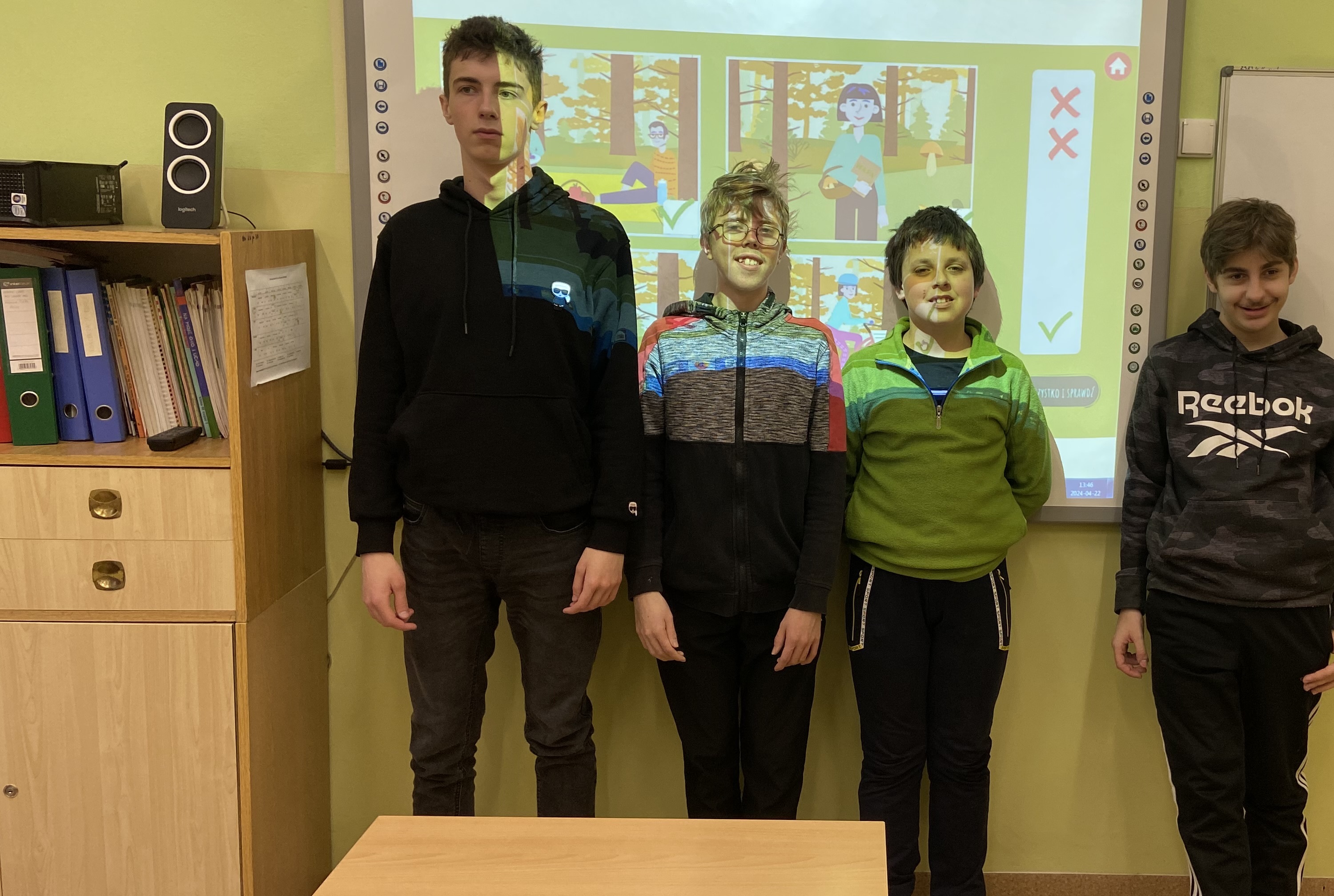 Uczniowie stoją na tle tablicy interaktywnej z wyświetlonym tematycznym slajdem.
