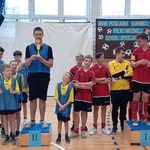 Uczniowie biorący udział w turnieju. Z przodu dwóch uczniów z pucharami na podium.