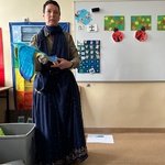 Nauczycielka w długiej sukience trzyma w rękach kawałek niebieskiej tektury,