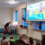 Uczniowie siedzący na ławkach oglądają film wyświetlany na ekranie.