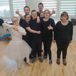 Uczennica w białym stroju królewny stoi obok grupy uczniów w czarnych kostiumach.