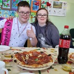 Jubilat z koleżanką siedzą za stołem na którym stoją talerze z pizzą.