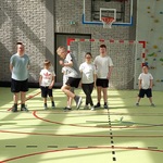 Na sali gimnastycznej grupa uczniów patrzy jak kolega podskakuje do góry w trakcie gry w szczura.