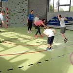 Grupa uczniów i nauczycielki grają na sali gimnastycznej w skakańca.