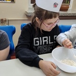 Uczniowie przyglądają się koledze wsypującemu miarkę mąki do miski.