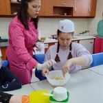 Uczennica miesza ciasto w misce. Prowadząca jej pomaga.