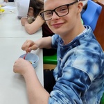 Uczeń siedzi przy stole i miesza łyżką składniki w misce.