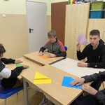 Uczniowie siedzą przy stolikach i składają kolorowe kartki.