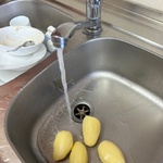 Obrane ziemniaki leżą w jednej komorze zlewu. Z kranu leci strumień wody.