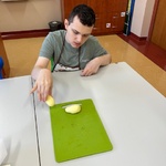 Uczeń siedzi przy stole i kladzie obranego ziemniaka na zieloną deskę.