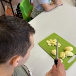 Uczeń z pomocą nożem kroi ziemniaka na desce do krojenia.
