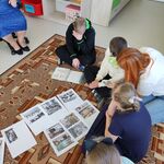 Uczniowie siedzą na dywanie. przed nimi leżą kartki z wydrukowanymi starymi zdjęciami.