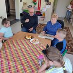Uczniowie oraz zaproszeni babcia Marysi  i dziadek Bartka siedzą wokół stołu przykrytego serwetką w kratkę. Na stole stoją talerze z ciastkami.