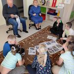 Zaproszeni babcia Marysi i dziadek Bartka siedzą na krzesłach. Przed nim na dywanie siedzą uczniowie.