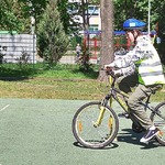 Boisko szkolne. Uczeń w odblaskowej kamizelce i kasku na głowie jedzie rowerem.