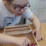 Uczennica siedzi przy stole i tka na krosnach
