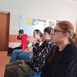 Uczniowie siedzą na krzesłach i oglądają film.