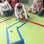 Sala gimnastyczna. Uczniowie siedzą na podłodze i grają w kapsle na torze wyklejonym taśmą.