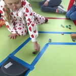 Sala gimnastyczna. Uczniowie siedzą na podłodze i grają w kapsle na torze wyklejonym taśmą.