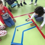 Sala gimnastyczna. Uczniowie siedzą na podłodze i grają w kapsle na torze wyklejonym taśmą.