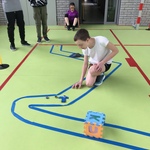 Uczeń gra w kapsle na torze wyklejonym niebieską taśmą na podłodze.