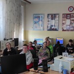 Grupa uczniów siedzi na fotelach w pracowni komputerowej.
