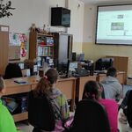 Grupa uczniów siedzi na fotelach w pracowni komputerowej o ogląda webinar wyświetlany na ekranie.