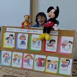 Za tablicą z kolorowymi obrazkami pani pedagog szkolna rozmawia z pacynkami.
