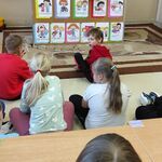 Uczniowie siedzą na podłodze i oglądają scenkę prezentowaną przez panią pedagog z użyciem pacynek
