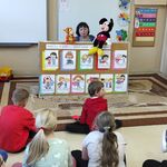 Uczniowie siedzą na podłodze i oglądają scenkę prezentowaną przez panią pedagog z użyciem pacynek.