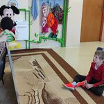 Uczniowie siedzą na podłodze i oglądają scenkę prezentowaną przez panią pedagog i kolegę z użyciem pacynek.