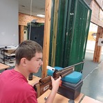 Uczeń siedzi przy stanowisku strzelniczym, w ręku trzyma karabinek