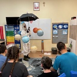 Uczniowie patrzą na nauczycielkę przebraną za astronautkę i kręcące się wokół niej planety.